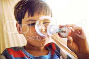 The simple things in life fascinate him. Shot of a curious little boy holding up and looking through a bubble he just blew outside during the day.