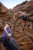 Its all about trust - belaying. Two female rock climbers scaling a rock face.