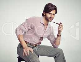 Groovy cool. A young man with 70s style sitting in the studio and smoking a pipe.