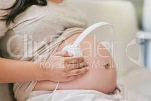 Enhance the stimulation of your unborn babys growing brain. Shot of a woman wearing headphones over her pregnant belly.