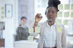 Noting her customers main concerns. Shot of a young businesswoman wearing a headset while brainstorming with notes on a glass wall in an office.