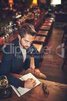 It all starts with a plot. High angle shot of a young man sitting with his journal in a bar.