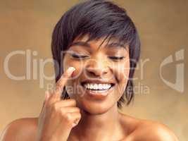 Now that is a deep cleanse. Studio shot of a beautiful young woman applying lotion to her cheek against a brown background.