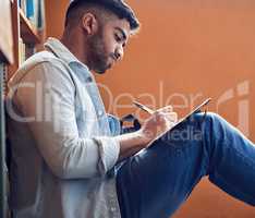 An investment in knowledge pays the biggest dividends. Shot of a young man making notes in a library at university.