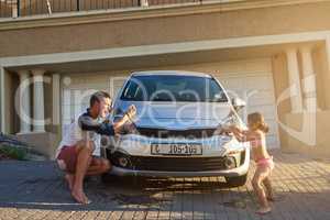 Fatherhood and childhood. Shot of a father and daughter having fun while washing a car.