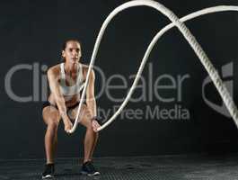 Getting ready for battle. Studio shot of an attractive young woman working out with heavy ropes against a dark background.