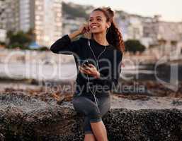 Raising my vibration through frequency music. Shot of an attractive young woman sitting alone on the beach after yoga and listening to music.