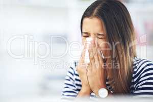 Its allergy season again. Shot of a young woman with allergies sneezing into a tissue at home.