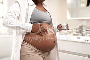 Giving her baby bump some moisture. Closeup shot of a pregnant woman applying cream on her stomach at home.