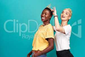 Who runs the world We do. Studio shot of a young woman putting a crown on her friend against a turquoise background.