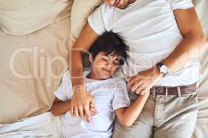 Hes sure to be having some sweet dreams. High angle shot of a little boy sleeping alongside his father in bed at home.