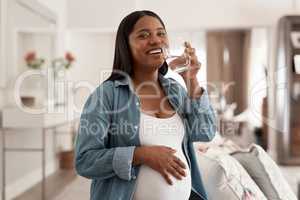 Got to stay hydrated for good health. Portrait of a pregnant woman drinking a glass of water at home.