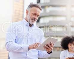 I can see what every team member is working on. Shot of a handsome mature businessman standing outside and using a digital tablet while his colleague stands behind him.