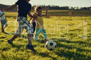 Fun with friends and a football. Shot of a group of children playing soccer together in a field outside.