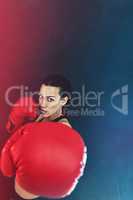 Knock them out. Shot of a young woman wearing boxing gloves against a dark background.