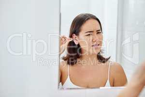 This is so uncomfortable. Shot of a young woman cleaning her ears with a cotton bud during her morning routine at home.