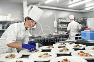 Making dinner into a masterpiece. Shot of a chef plating food for a meal service in a professional kitchen.