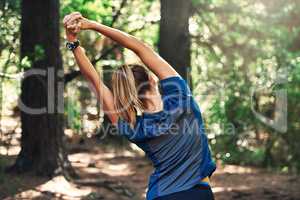 Getting in a good stretch before her run. Shot of a young woman warming up for a trail run.