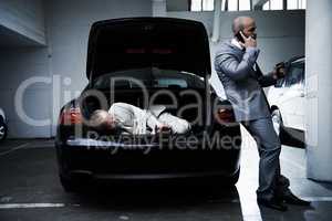 Hostage to the mob. A frightened businessman lying in the trunk of a car while his armed captor talks on a cellphone.