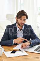 Punctuality is crucial in this office. A handsome businessman pointing to his watch while at his desk.