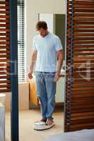 Weigh yourself every day. Shot of a young man weighing himself on a scale in his bathroom.