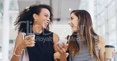 Good times in the office. Cropped shot of two young businesswomen chatting and using a smartphone while walking in an office on a coffee break.