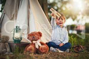 Soaring high above the clouds. Shot of a cute little boy playing with a toy airplane while sitting outside his teepee.