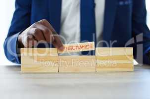 Good cover for a good life. Shot of an unrecognisable businessman assembling wooden blocks the word insurance on them.