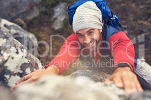 The view will be worth the effort. Shot of a happy hiker climbing over rocks on a mountain trail.