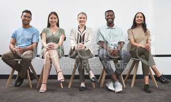 Confident and keen to prove their talent. Portrait of a group of businesspeople sitting together in a line against a white wall.