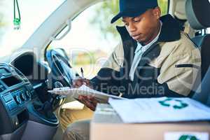 Ive got just a few more stops to make. Shot of a courier writing on a clipboard while sitting in a delivery van.