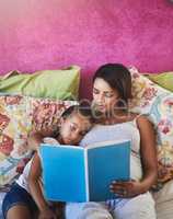 Give them the chance to explore many wonderful worlds. Shot of a mother reading a story to her little daughter at home.