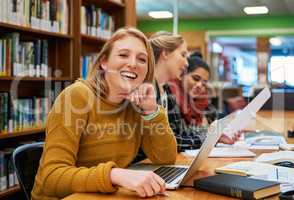 She is certain that she will pass the test. Portrait of a cheerful young female student working on her laptop and studying inside of a library.