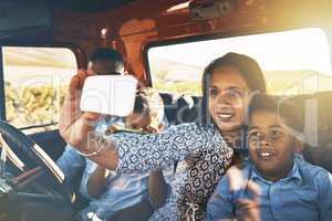 Time for some photos for the memories. Shot of a cheerful young family driving in a red pickup truck on a rural road while taking a self portrait on a cellphone together.