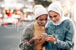 Check the maps. Cropped shot of two attractive young women wearing headscarves and standing together while using a cellphone in the city.