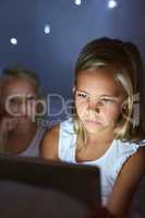 Bedtime in the age of the app. Shot of two little girls using a digital tablet before bedtime.