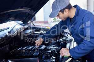Giving your engine a once over. High angle shot of a handsome young male mechanic working on the engine of a car during a service.