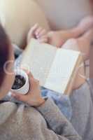 Her weekend is all booked. Cropped shot of a woman relaxing with a book and cup of coffee at home.