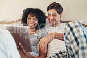 Time to wake up the rest of the world. Shot of an affectionate young couple using a digital tablet while spending time together in bed at home.
