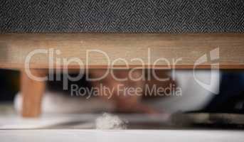 Urgh, I left some dirt. Shot of an unrecognizable woman finding a ball of dust under the sofa in the living room at home.