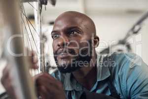 Whys it still crooked. Shot of a handsome young man crouching in his shop and repairing a bicycle wheel.