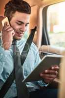 Managing business on the go. Shot of a young businessman talking on a phone while using a digital tablet in the back seat of a car.