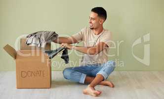 Donating some of my old clothes. Shot of a young man putting clothes into a donation box at home.