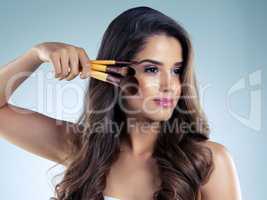 Enhance your beautiful face. Studio shot of a beautiful young woman holding cosmetic brushes against a blue background.