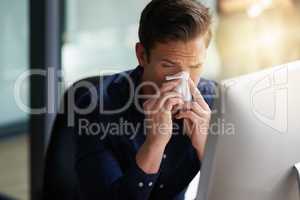 This cold is starting to torture me. Shot of a young businessman blowing his nose in an office.