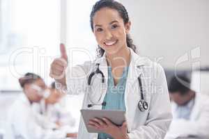 I approve. Cropped portrait of an attractive young female doctor giving thumbs up and using a tablet while standing in the boardroom with her colleagues in the background.