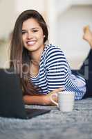 Wireless lets me browse anywhere at home. Portrait of a smiling young woman lying on the floor at home using a laptop.