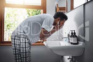 Freshening up. Cropped shot of a handsome young man washing his face in the bathroom at home.