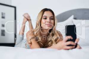 A selfie a day keeps the boredom at bay. Shot of a young woman using her cellphone while lying on her bed.