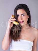 I might be going bananas because I cant hear you. Studio portrait of an attractive young woman pretending to use a banana as a phone against a purple background.